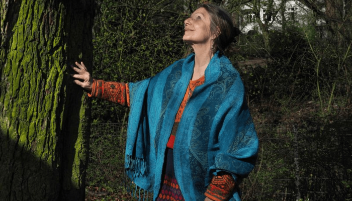 Elita Carstens in der Natur, Hand an einem Baum, nach oben schauend