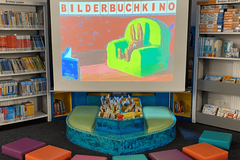 Eine Leinwand mit dem Slogan "Bilderbuchkino", davor bunte Sitzkissen