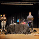 Vier Personen führen auf einer Bühne ein Hörspiel auf.