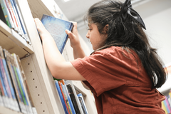 Mädchen stellt Buch in Regal ein