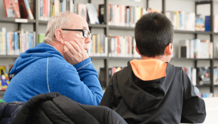 Mann hilft Kind beim Lesen lernen in der Bücherhalle