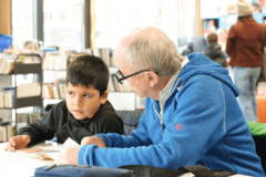 Mann hilft Kind beim Lesen lernen in der Bücherhalle