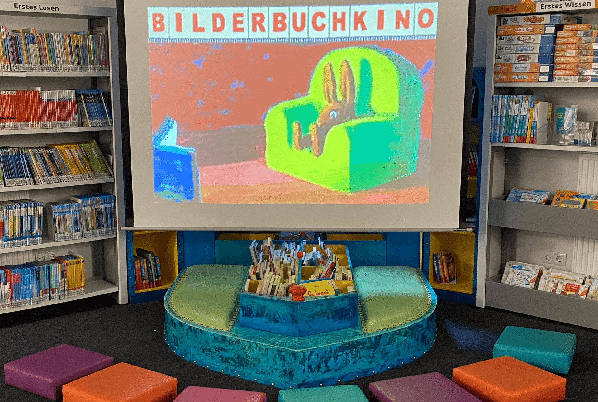 Eine Leinwand mit dem Slogan "Bilderbuchkino", davor bunte Sitzkissen