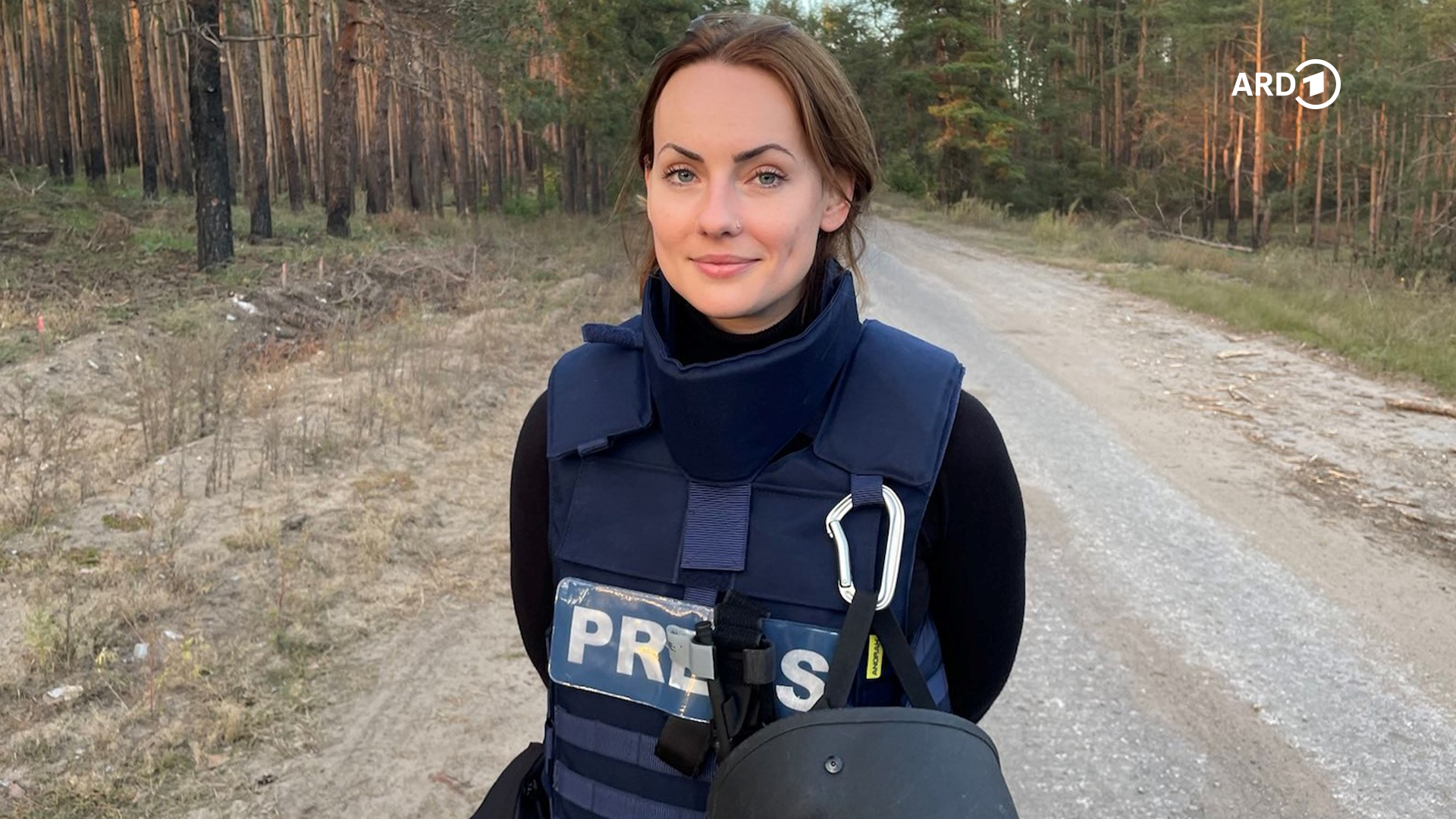 lächelnde jüngere Dame steht in Sicherheitskleidung der Presse auf einem Waldweg